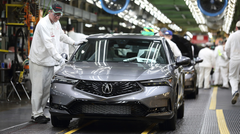 A worker wears gloves to touch a gray Acura Integra being built.