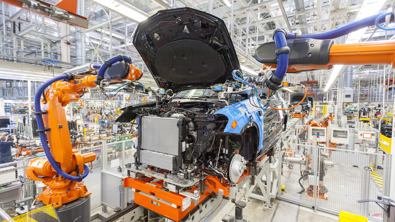 A vehicle is assembled in a modern BMW plant with orange robotic arms.