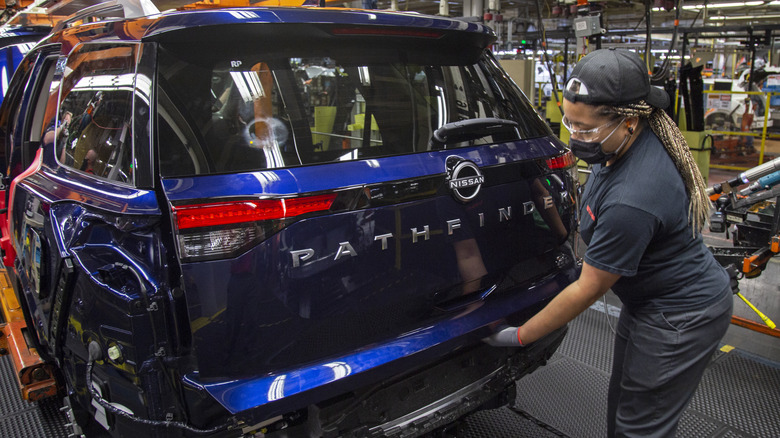 A person works on a blue Nissan Pathfinder in a factory.
