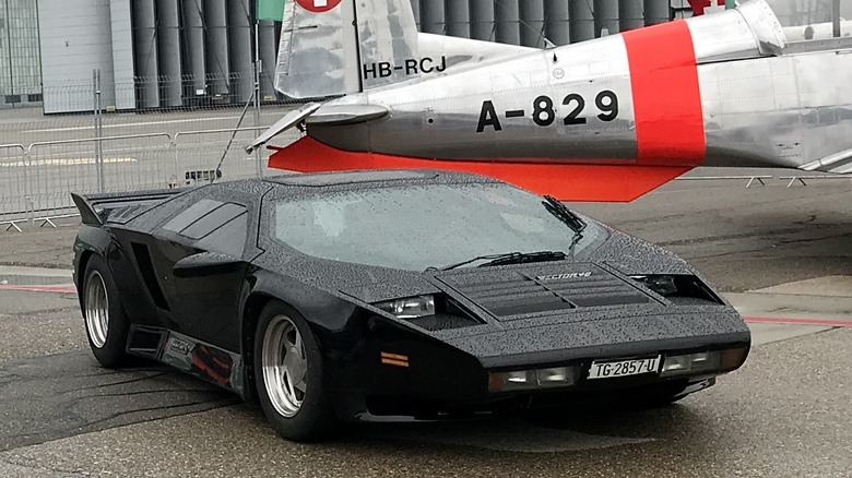 A black Vector W8 in front of a plane.
