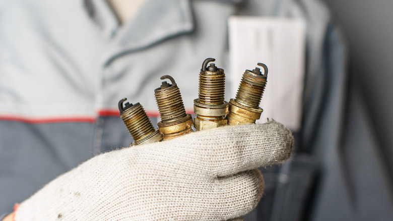 A mechanic holding four used spark plugs