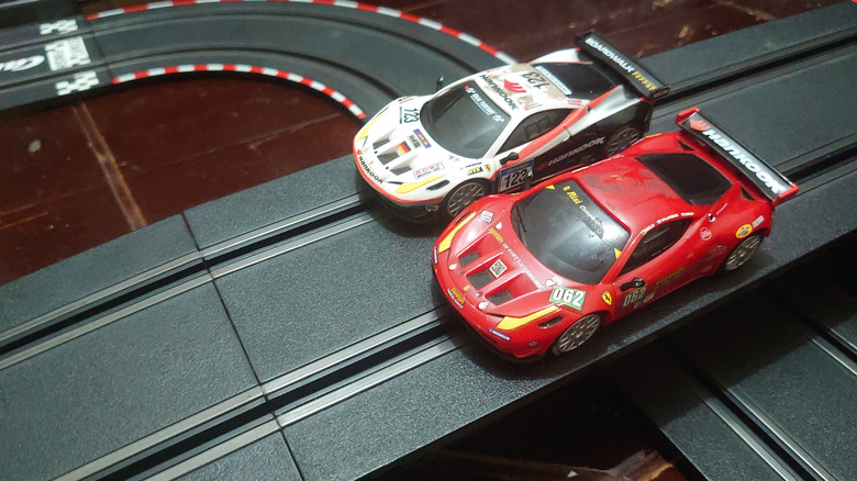 Two Ferrari slot cars side by side, one red and the other white.