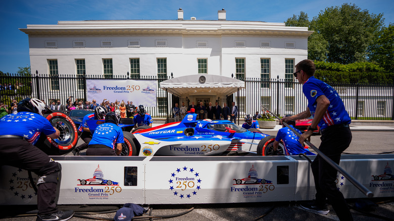 U.S. President Donald Trump and others watch as IndyCar series driver David Malukas drives his race car towards a pit crew to perform a tire change during a Freedom 250 Grand Prix showcase on West Executive Avenue between the West Wing of the White House and the Eisenhower Executive Office Building on July 13, 2026 in Washington, DC.