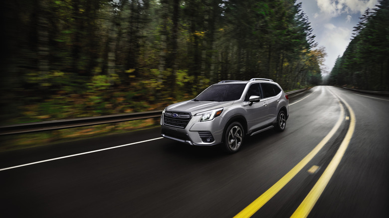 Front 3/4 view of a 2024 Subaru Forester driving down a road in a forest