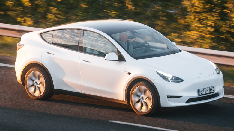 A white Tesla Model Y is in motion on the highway.