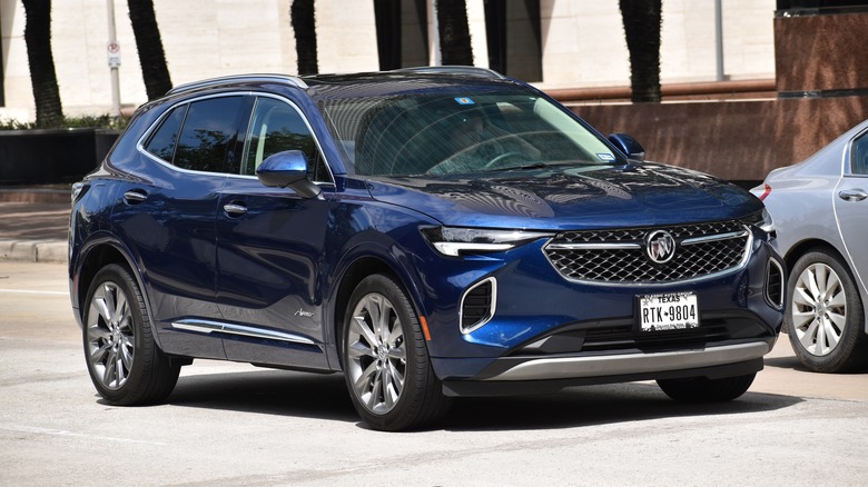 A blue Buick Envision drives through a city.