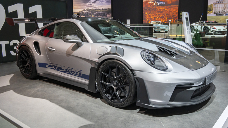 A silver 2023 Porsche 911 GT3 RS with black accents in a showroom setting in Brussels, Belgium.