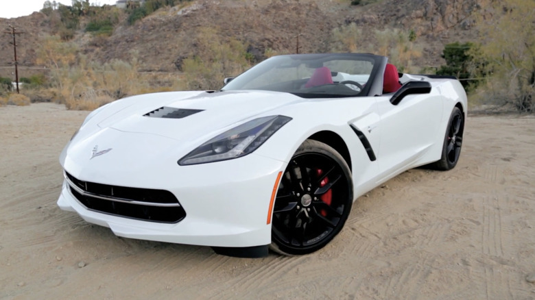 A white 2014 Chevrolet Corvette Stingray Z51 Convertible with red seats and the top down on a dirt road.