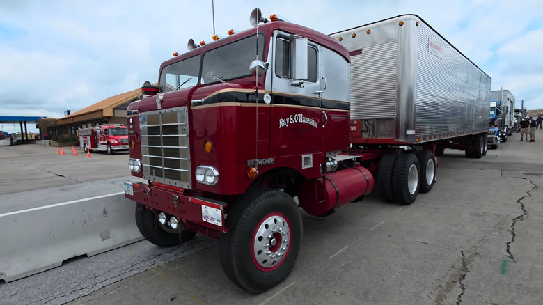 A maroon and silver Kenworth "Bullnose" COE semi truck parked on a concrete tarmac.