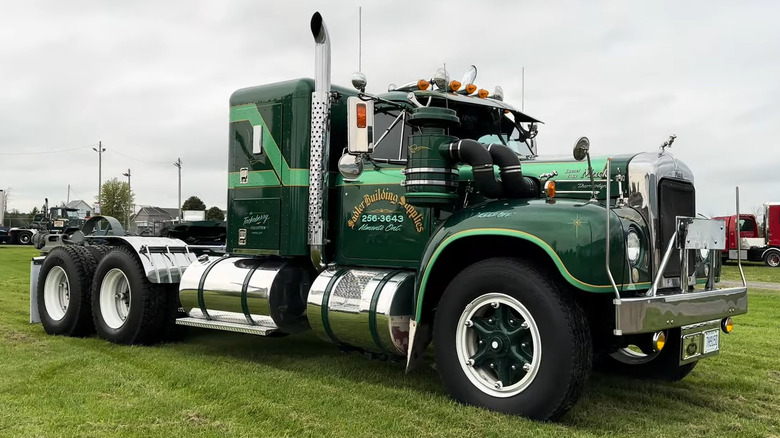 A pristine dark green Mack B-61 conventional semi truck with vibrant lime-green accent striping parked on grass.