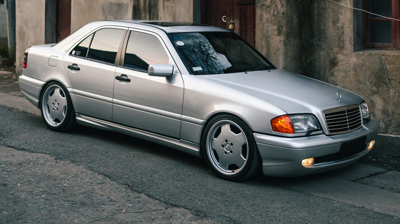 A silver W202 Mercedes-AMG C43 sedan sits on a city street in front of a concrete building