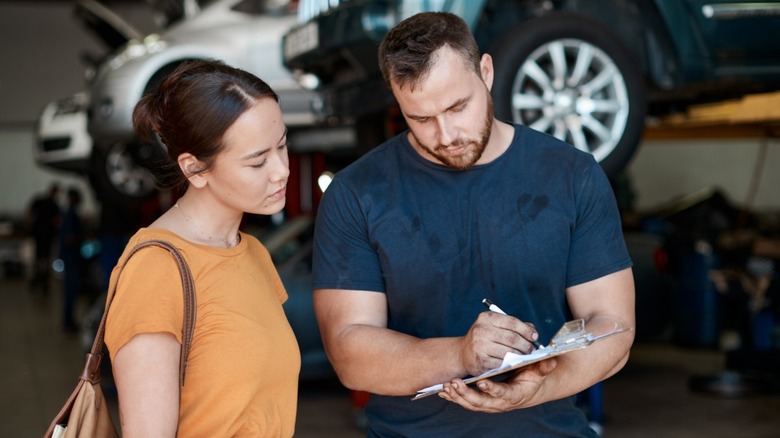 A mechanic going over a bill with a customer with cars on lifts in the background