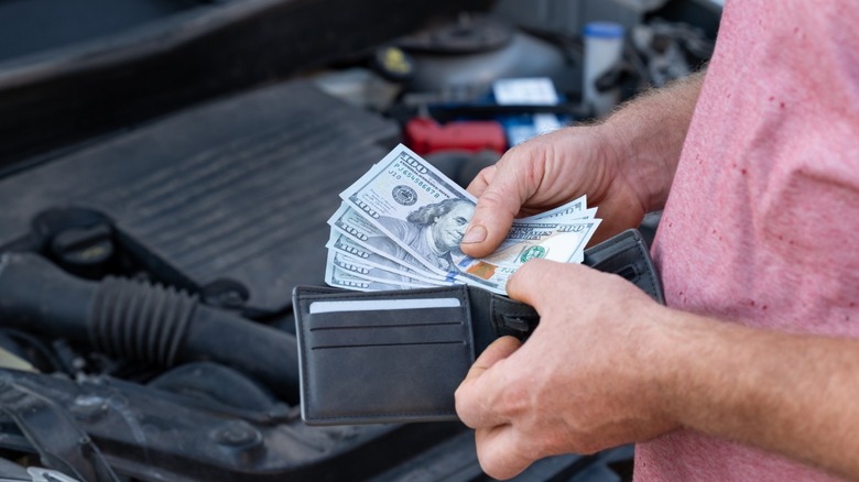 A person standing in front of an open car hood takes $500 out of their wallet