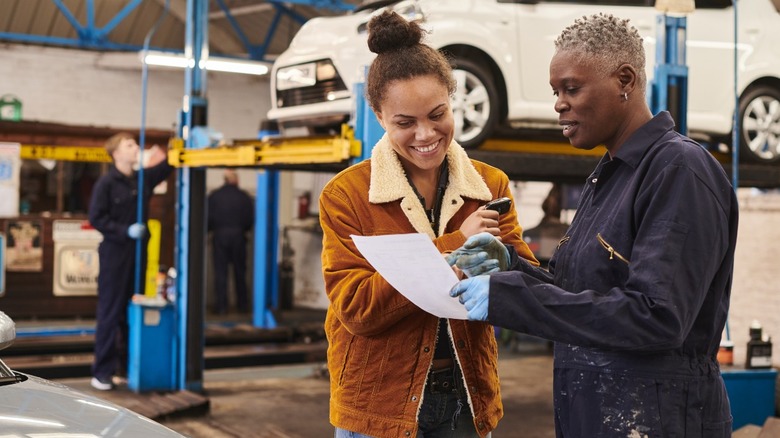 A mechanic going over a car repair bill with a customer with a vehicle on a lift in the background