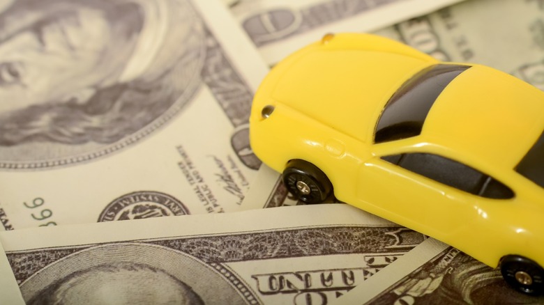 A yellow toy car sits on top of $100 bills