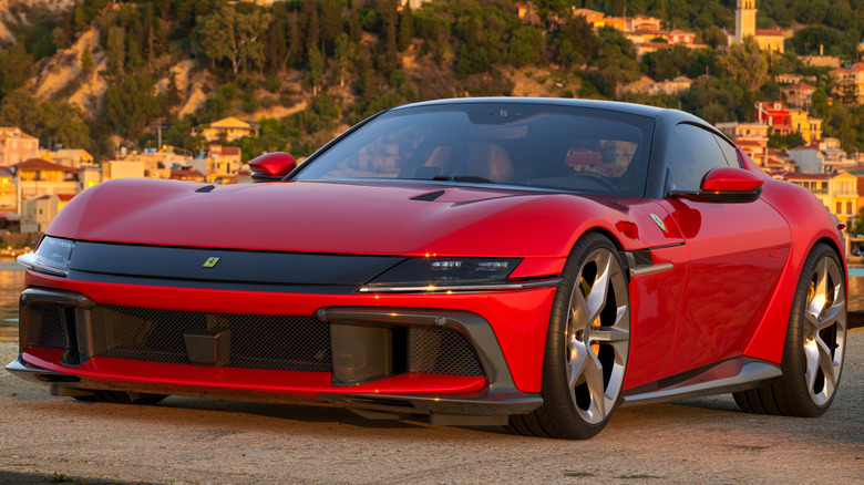 A close-up of a red Ferrari 12 Cilindri parked near an old town.
