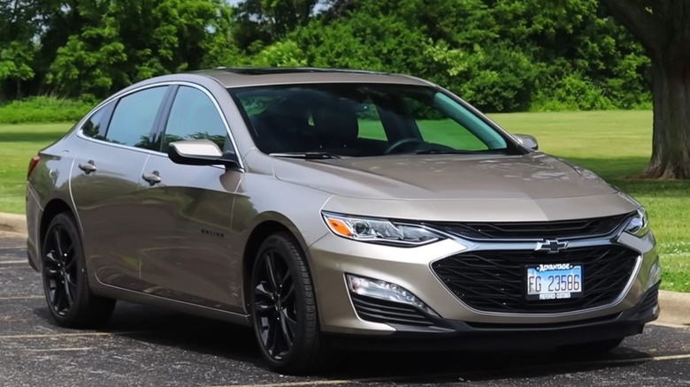 2025 Chevrolet Malibu LT parked on a paved surface with trees and lush green grass in the background