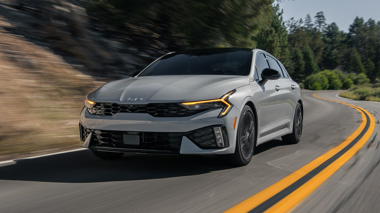 2025 Kia K5 driving down a road with trees in the background
