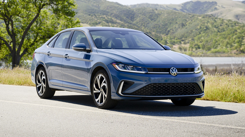 Front 3/4 static shot of a 2025 Volkswagen Jetta on a paved road with trees and hills in the background
