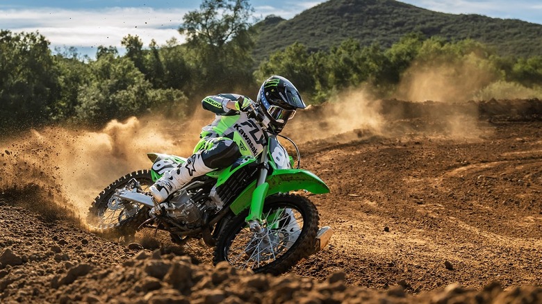 A high-action motocross shot of a 2026 Kawasaki KX112 navigating a sharp, rutted berm on a dirt track.