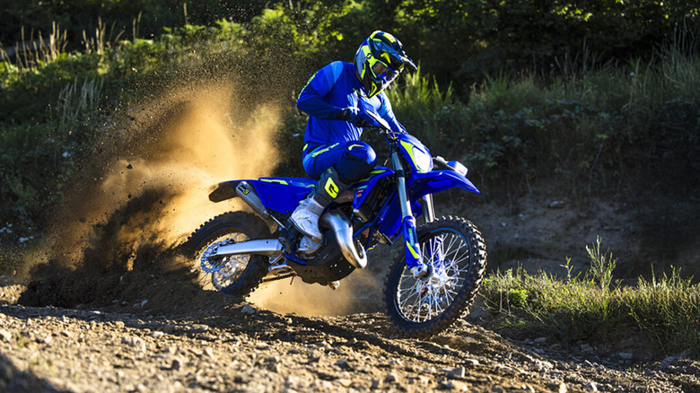 A blue 2026 Sherco 125 SE Factory enduro bike power-sliding through a dusty trail.
