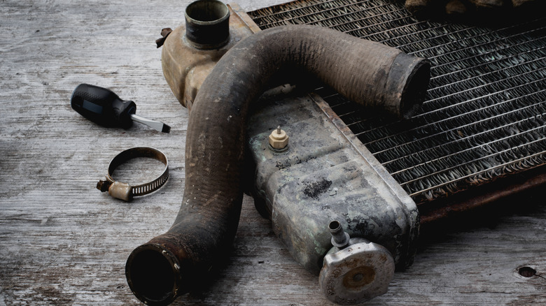 An old and rusted radiator and worn cooling hose on a table at the workshop
