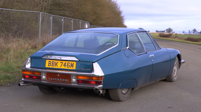 A blue Citroën SM is parked near a fence