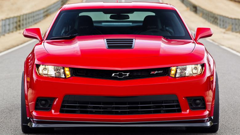 A close-up front view of a red 2015 Chevrolet Camaro Z/28 parked on a narrow country road
