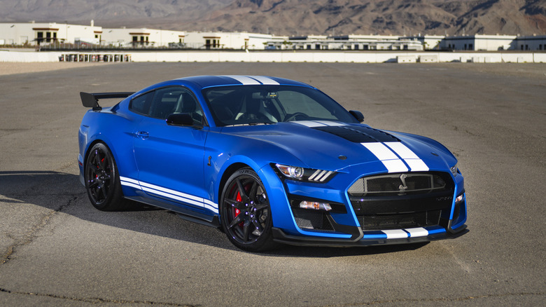 A 2020 Shelby GT500 in blue with white center stripes parked on tarmac with mountains in background