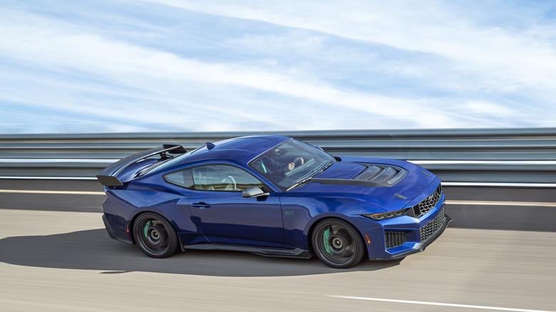 A blue Ford Mustang Dark Horse SC with Track Pack driving next to a guardrail