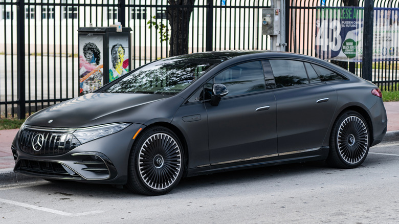A grey Mercedes-Benz EQS parks next to a fence.