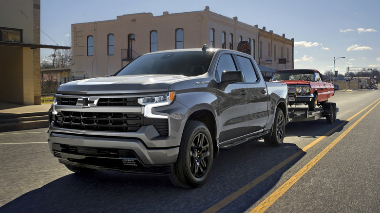 A 2026 Chevrolet Silverado towing a car behind it on a road