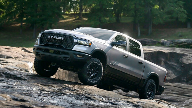 A gray Ram 1500 driving up rocks in a wooded area