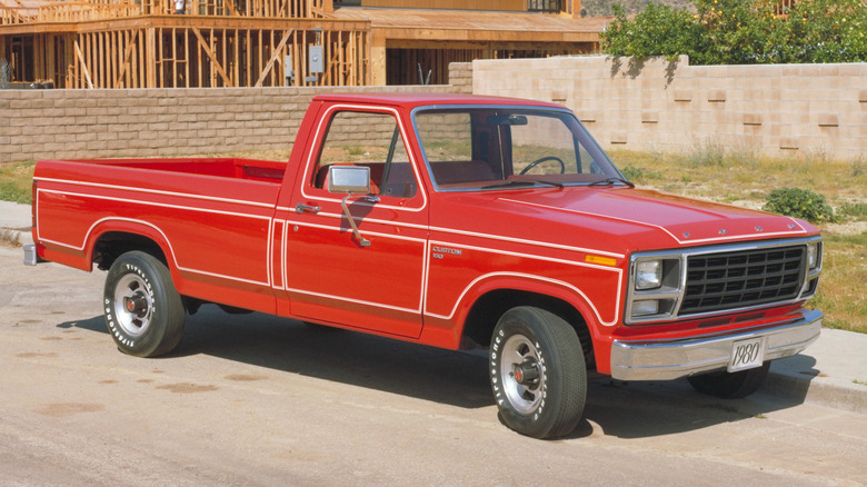 A bright red 1980 Ford F-150 Custom standing in front of an under-construction house in the sun.