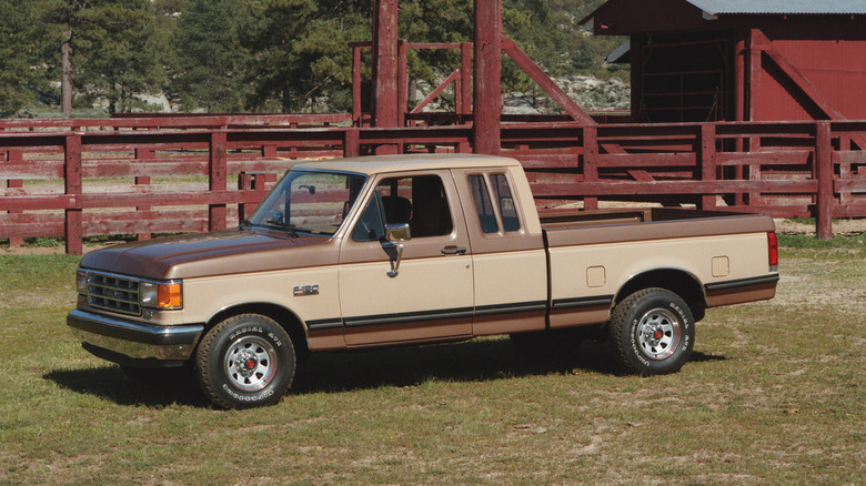 A beige and brown two-tone 1987 Ford F-150 in the SuperCab configuration pictured on a farm here.