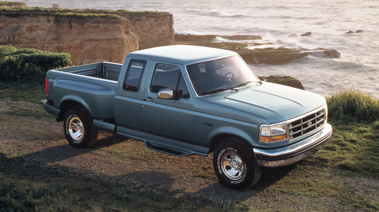 A light blue 1994 Ford F-150 SuperCab pickup with the flareside bed style standing on a cliff next to the sea.