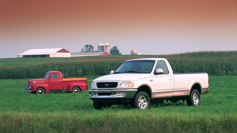 A white 1998 Ford F-150 Lariat standing in a field with a red 1948 Ford F-1 pickup in the background.