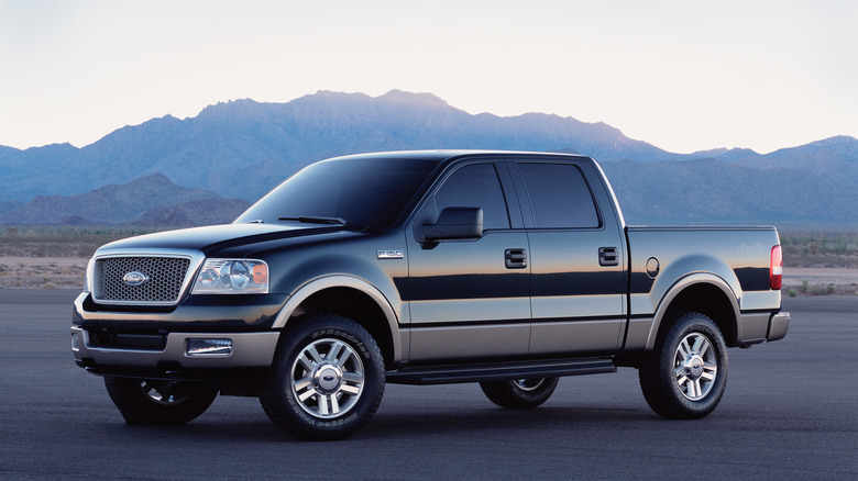 A black metallic finished 2004 Ford F-150 in the then-new facelifted style standing on asphalt with mountains in the back.