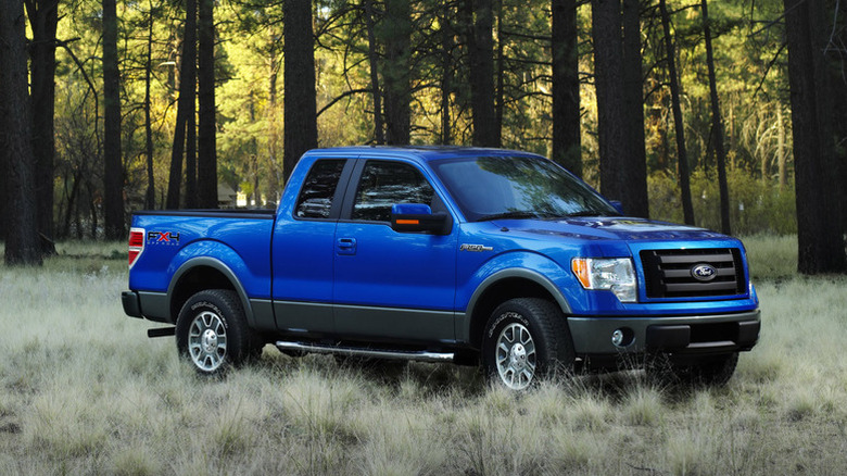A 2009 Ford F-150 finished in a dark metallic blue colorway standing in a clearing with a forest visible further afield.