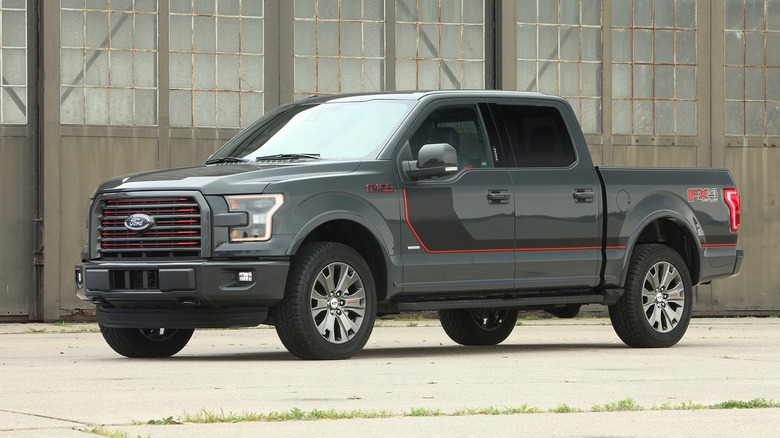 A grey 2015 Ford F-150 Lariat Sport with a red body line standing in an industrial area on a sunny afternoon.