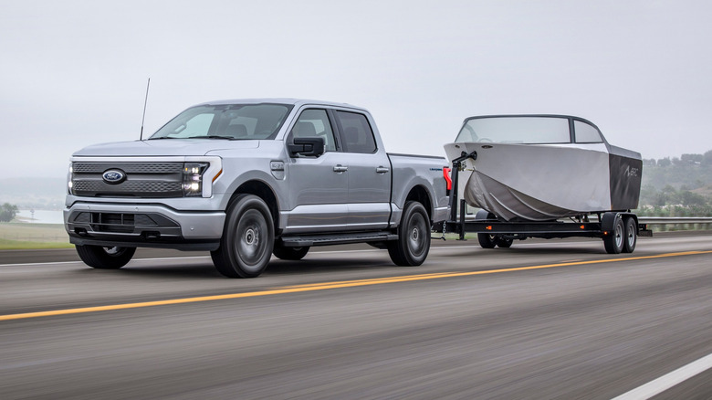 A silver 2025 Ford F-150 Lightning XLT towing a boat down a motorway at speed on an overcast day.