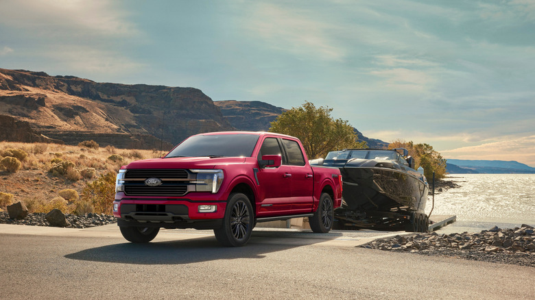 A red 2026 Ford F-150 Platinum pulling a boat up a boat launch, with mountains and a lake in the background