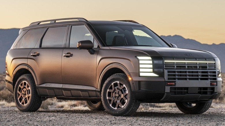 A boxy 2026 Hyundai Palisade SUV finished in matte bronze parked on a gravel clearing in a desert landscape during twilight.