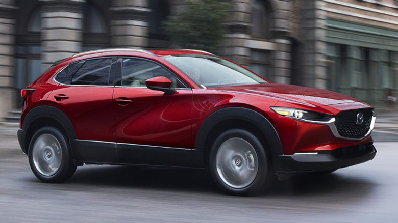 A vibrant red Mazda CX-30 compact crossover driving along an empty city street.
