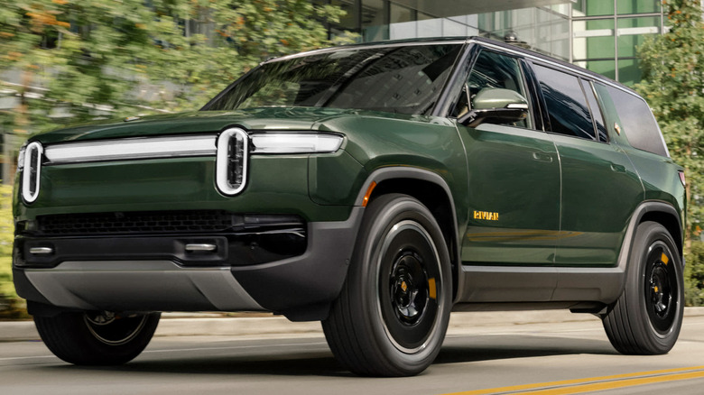 A dark green Rivian R1S luxury electric SUV driving on a clean city street.