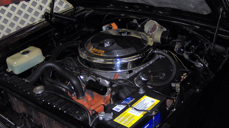 An original 426 Hemi engine sitting in the hood of a black 1966 Dodge Charger.
