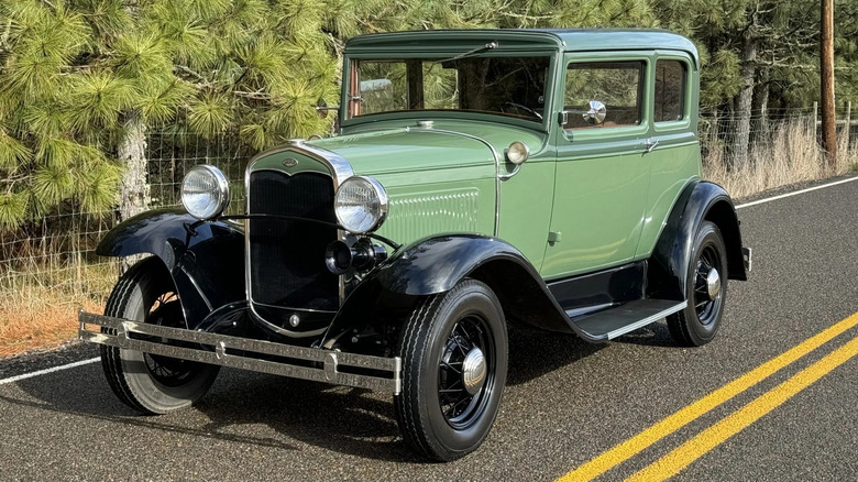 Front three quarters of a green Ford Model A parked on a street in front of trees