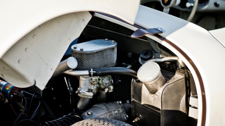 A detailed close-up inside the engine bay of a Porsche 550 Spyder engine bay, showcasing an early air-cooled flat-4 setup featuring a carburetor topped with a metal mesh air cleaner filter