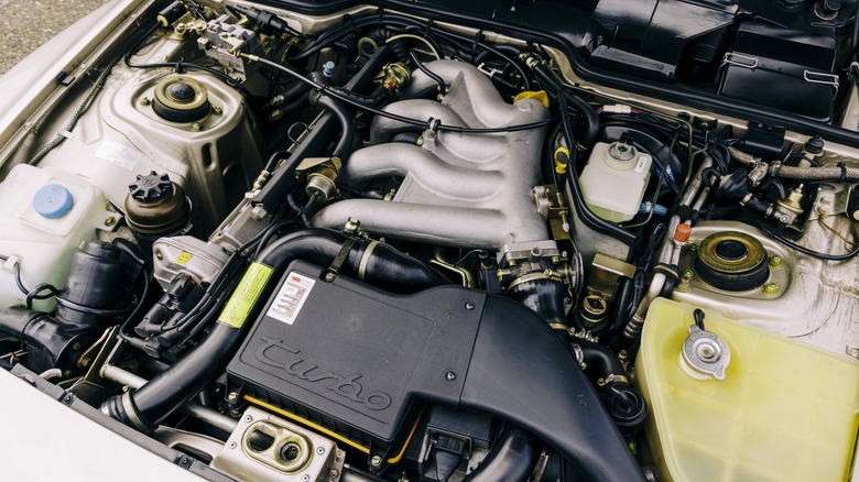 The clean front-engine bay of a classic gold Porsche 944 Turbo, showcasing its water-cooled inline-4 engine architecture