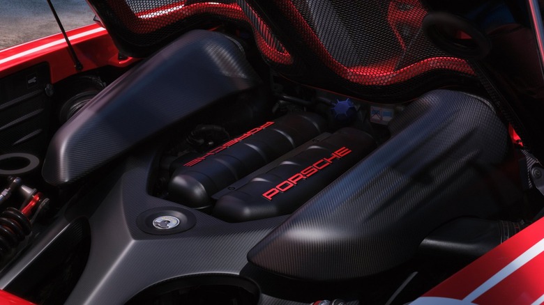 A high-angle, close-up shot of a red Porsche Carrera GT's engine bay, emphasizing the raw carbon fiber structural framing surrounding the black intake manifolds featuring the "PORSCHE" name painted in bright red script.